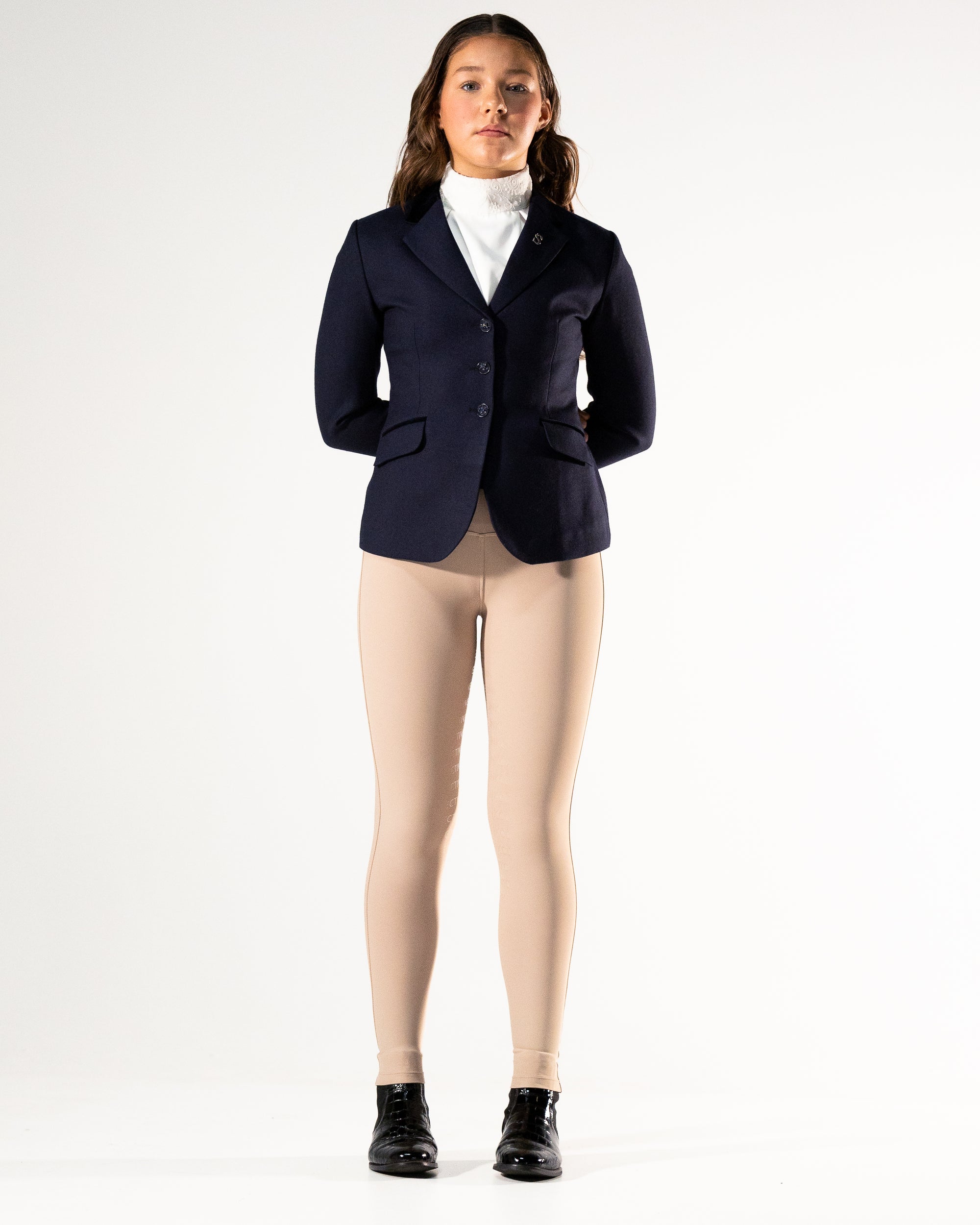 Person wearing a navy blazer, white shirt, beige leggings, and black boots on a white background