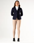 Person wearing a navy blazer, white shirt, beige leggings, and black boots on a white background