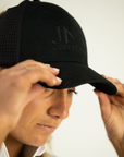Person wearing a black cap with 'JN Collection' logo on a plain background